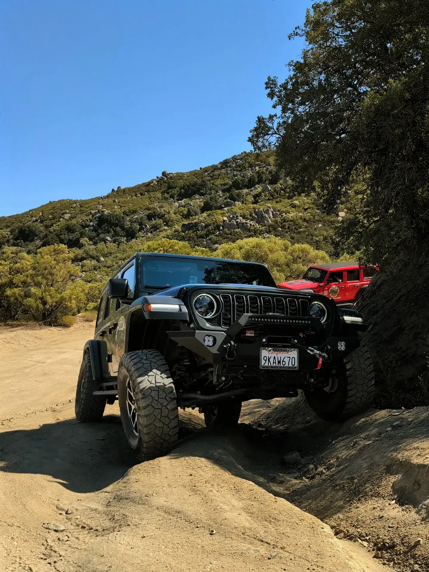 Black Jeep cresting a boulder with red Rubicon close behind on the Peaks & Pines route